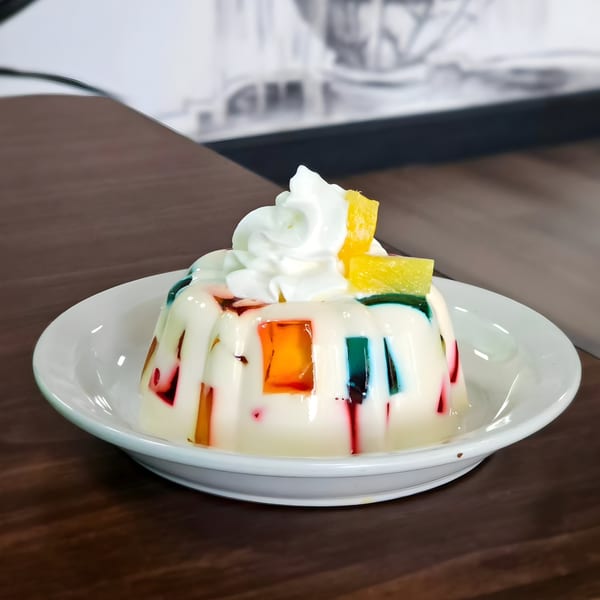 Mosaic gelatin dessert with whipped cream and pineapple on a white plate at Los Agaves Taqueria.
