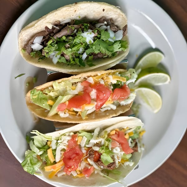 Three Los Agaves Taqueria tacos, one carne asada, two with ground beef, lettuce, cheese, and tomatoes.