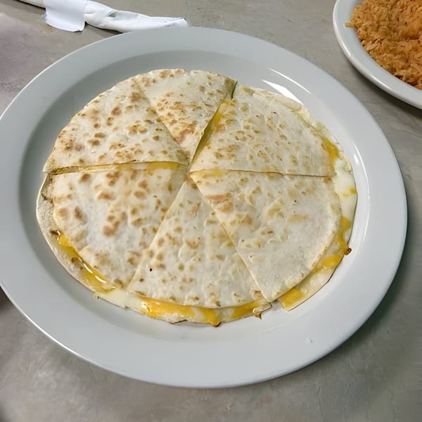 A cheese quesadilla, cut into six triangular pieces, on a white plate at Los Agaves Taqueria.