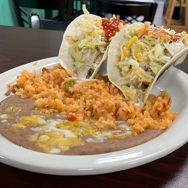 Two Los Agaves Taqueria tacos with rice and refried beans on a white plate.