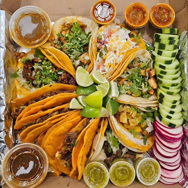 A large catering tray of Los Agaves Taqueria tacos, with various fillings, limes, cucumbers, and sauces.