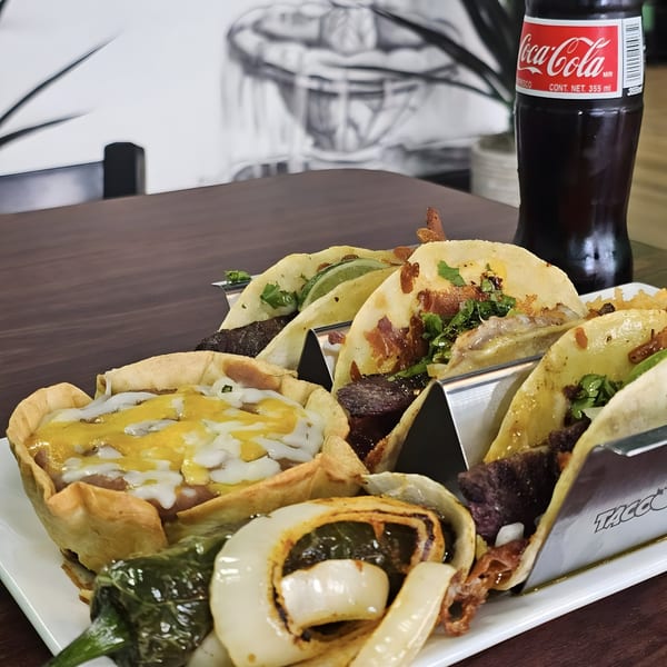 A plate of Los Agaves Taqueria tacos and a tostada with a Coca-Cola bottle in the background.