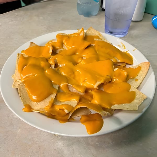 A white plate piled high with tortilla chips generously covered in melted yellow cheese sauce.